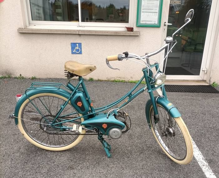 Un cyclomoteur vintage turquoise avec des pneus couleur crème devant le centre de contrôle.