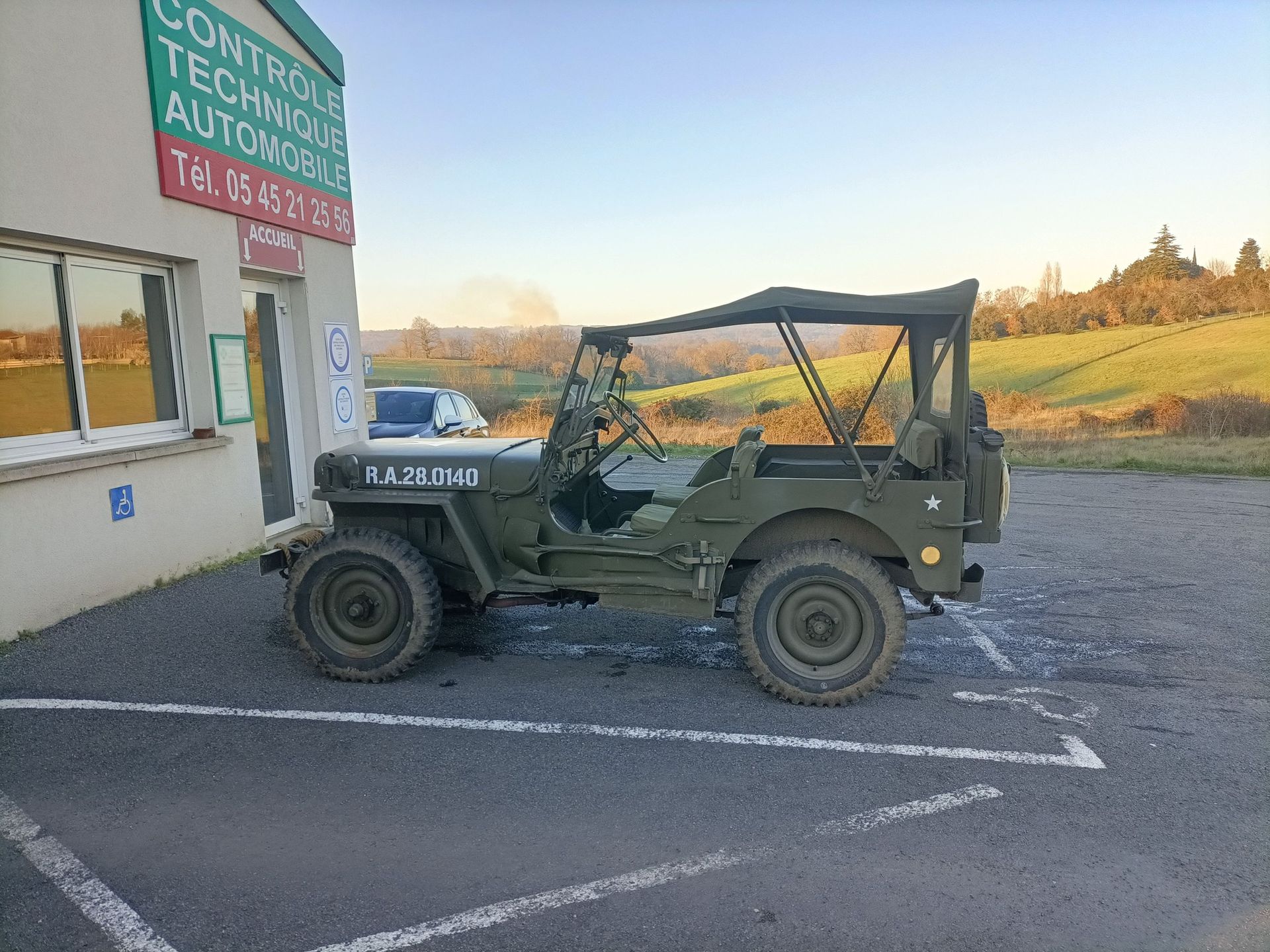 Jeep vintage verte garée devant un centre de contrôle technique.