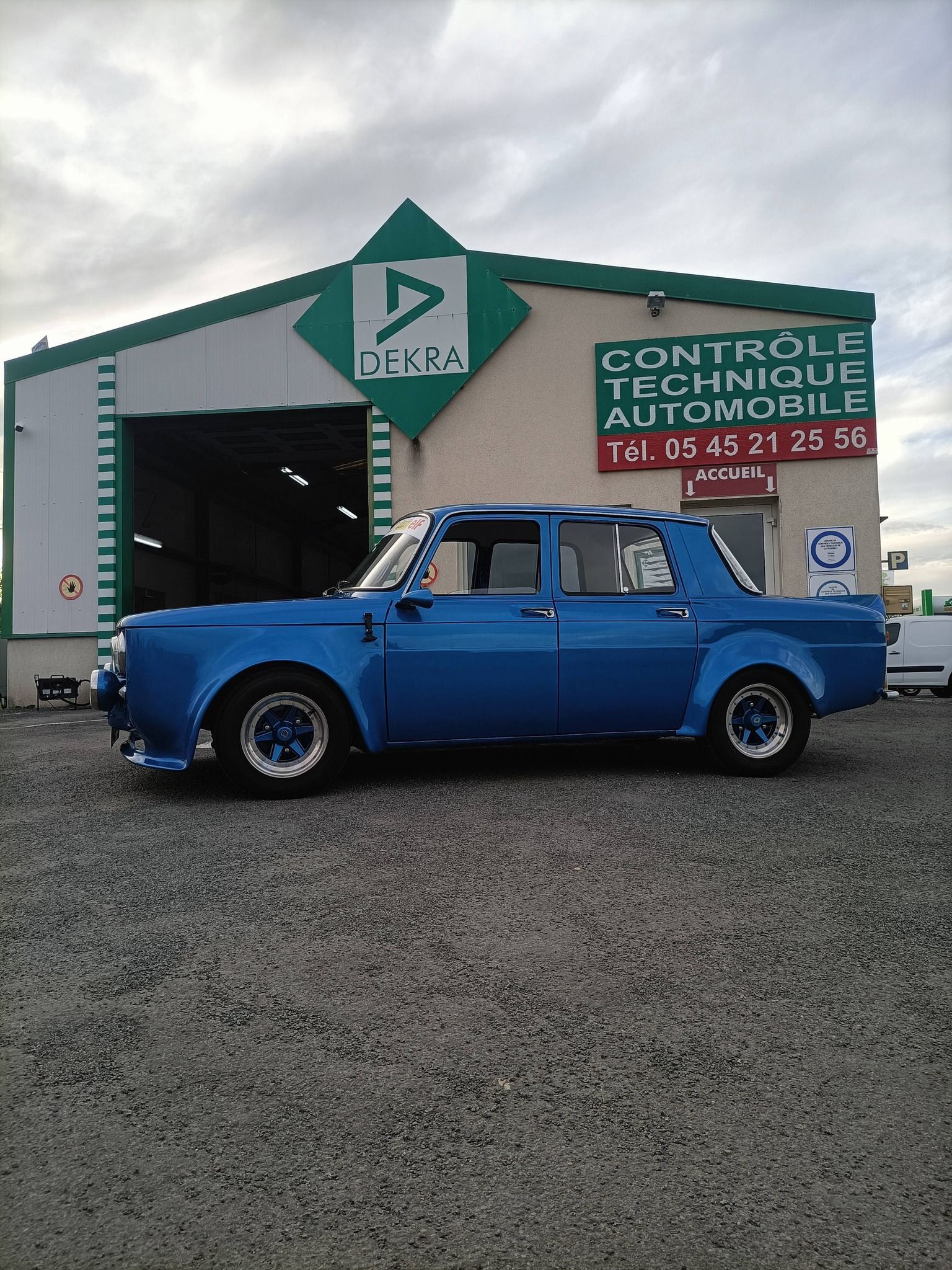 Voiture bleue garée devant un garage de contrôle technique.