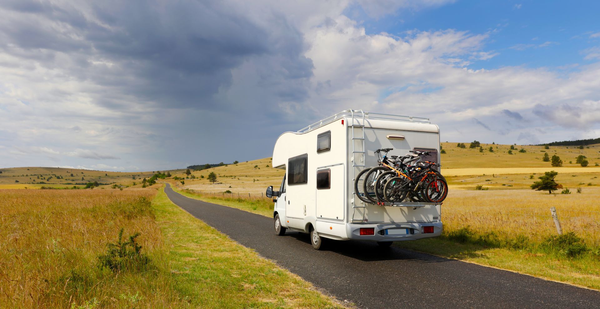 Un camping-car blanc roule sur une route de campagne. Des vélos sont attachés à l'arrière.