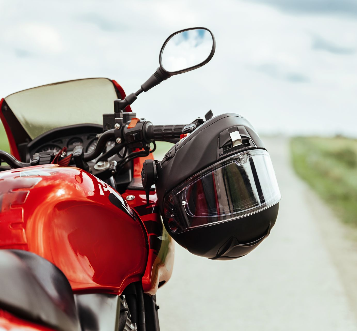 Une moto rouge avec un casque noir accroché au guidon, garée sur une route.
