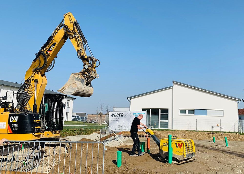 Ein Mann arbeitet mit einem gelben Bagger auf einer Baustelle.