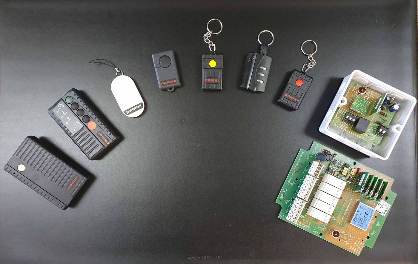 Diverse schwarze elektronische Torfernbedienungen, Schlüsselanhänger und Platinen auf einer dunklen Oberfläche.