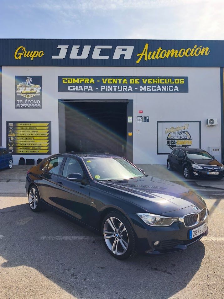 Sedán oscuro aparcado frente al concesionario de automóviles JCA Automoción, con carteles de servicio al fondo