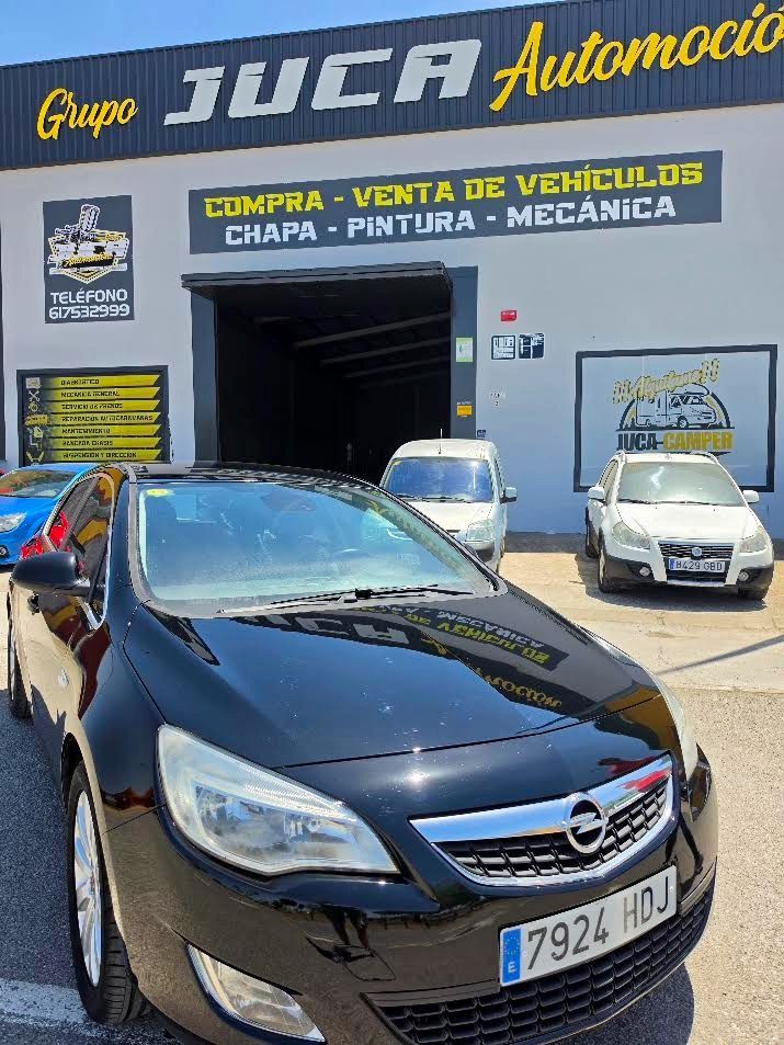 Coche negro aparcado frente a un taller de reparación de vehículos con un letrero azul y amarillo.