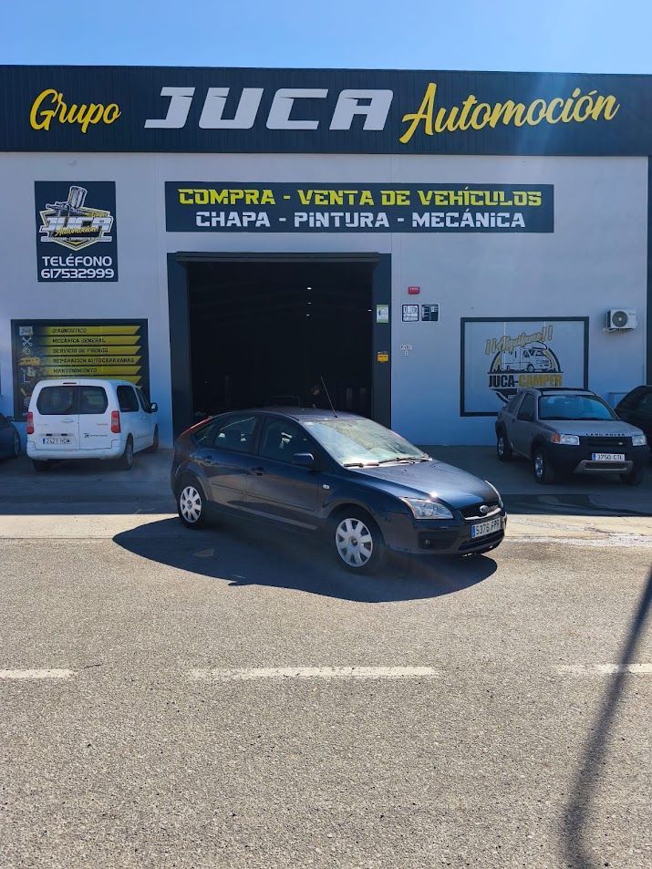 Concesionario de automóviles con dos coches estacionados: una berlina negra delante y un todoterreno oscuro a la derecha.