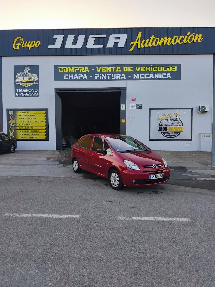 Coche rojo aparcado frente a la fachada de un taller de reparación de automóviles de Juca Automación.