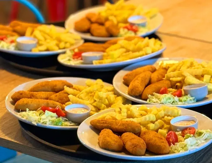 Interior de restaurante con mesas y sillas de madera, paredes de piedra y suelo de baldosas.