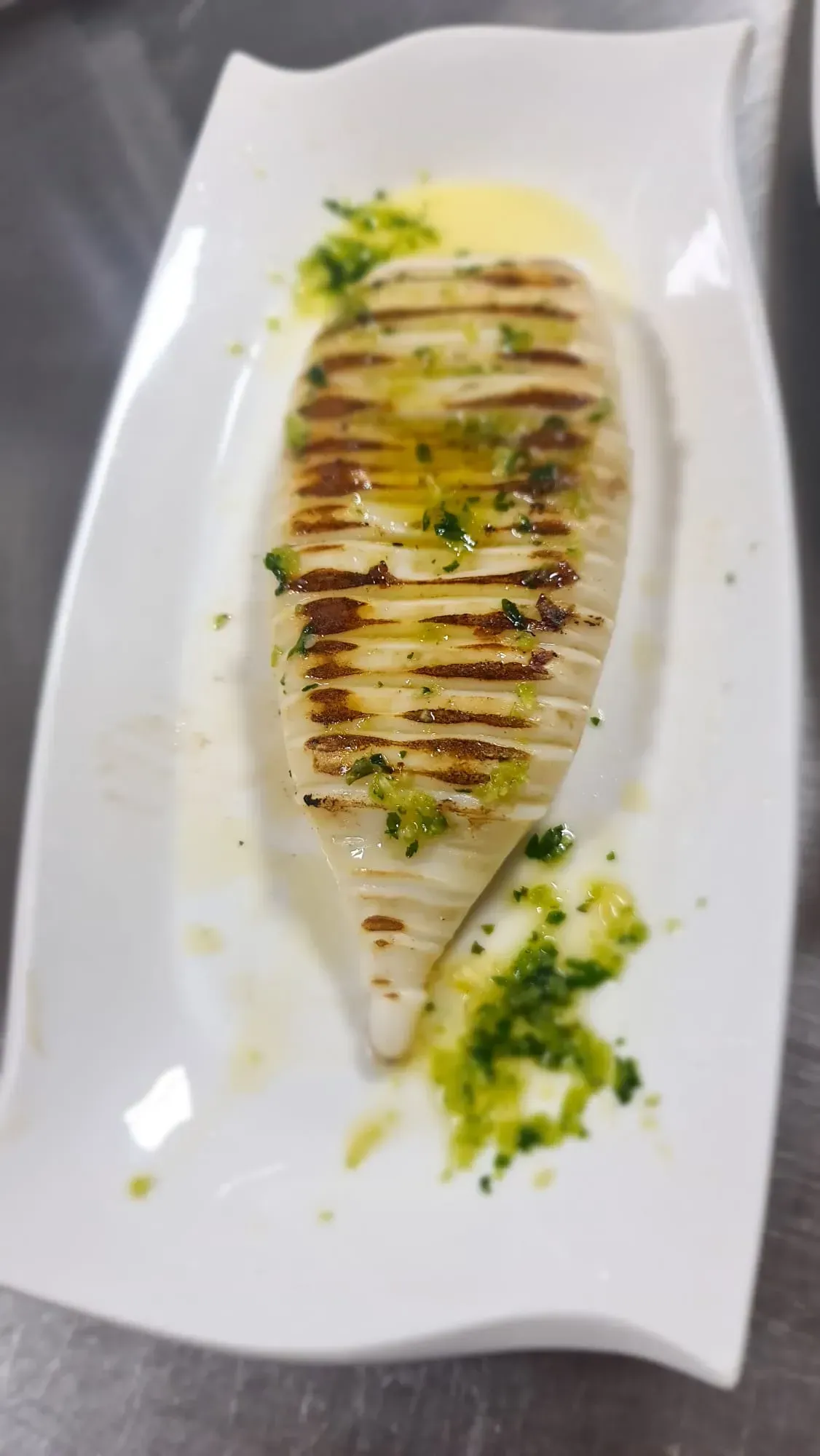 Un calamar entero a la parrilla con aceite de hierbas, servido en un plato rectangular blanco.