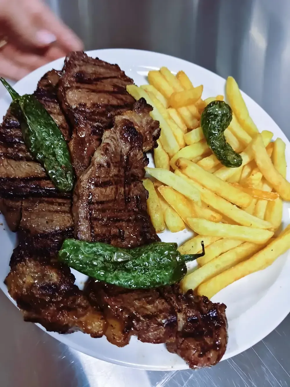 Un plato que incluye un filete a la parrilla adornado con pimientos verdes, servido junto con una guarnición de papas fritas doradas.