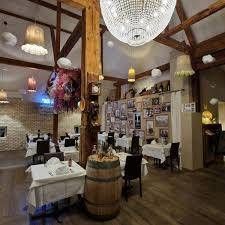 Ein elegantes Restaurantinterieur im rustikalen Stil mit weiss gedeckten Tischen, einem hölzernen Weinfass und Kronleuchtern.