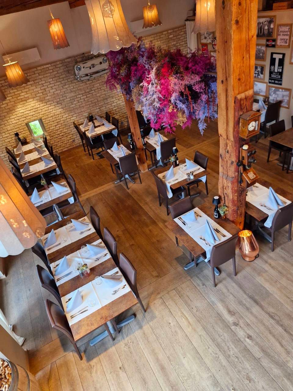 Eine erhöhte Ansicht des Restaurantinterieurs mit Holztischen, braunen Stühlen und hängenden Blumenarrangements.