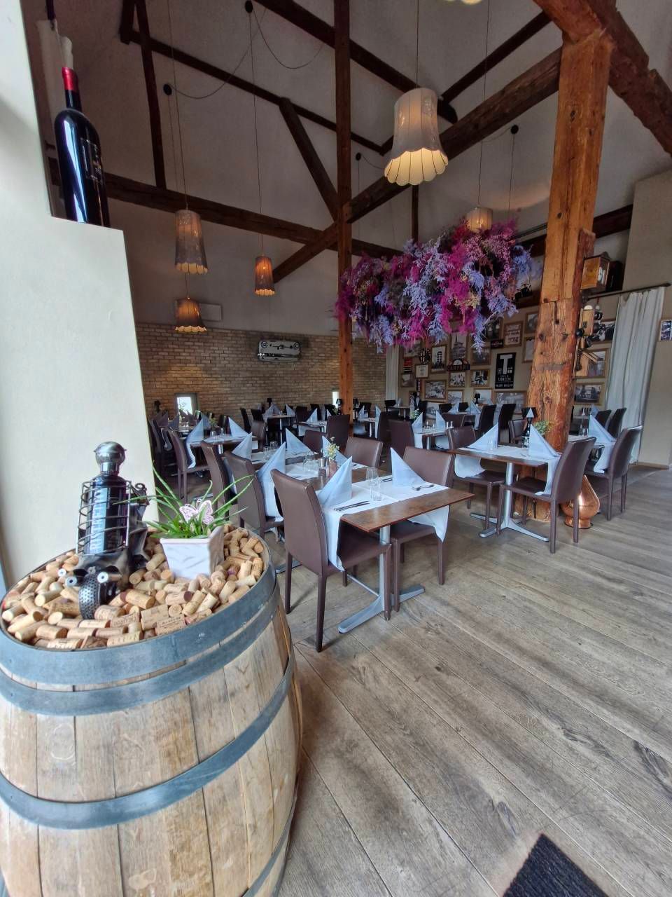 Ein rustikaler, luftiger Restaurant-Essbereich mit Holzbalken, gedeckten Tischen und einer grossen dekorativen Blumeninstallation.