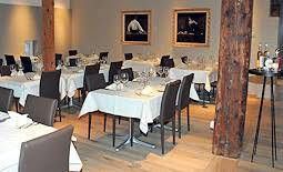 Das Interieur eines Restaurants mit weiss gedeckten Tischen, dunkelbraunen Stühlen, Holzsäulen und gerahmten Kunstwerken an den Wänden.