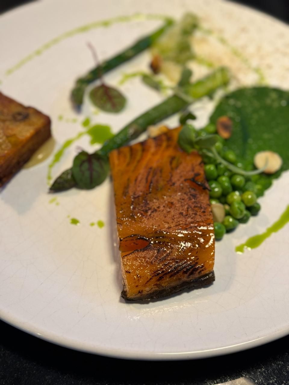 Gegrillter Lachs mit Spargel, Erbsen und grüner Sauce auf einem weissen Teller.