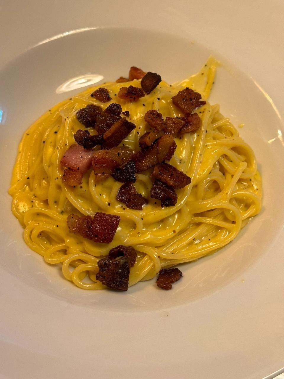 Spaghetti Carbonara mit cremiger gelber Sauce und knusprigem Speck auf einem weissen Teller.
