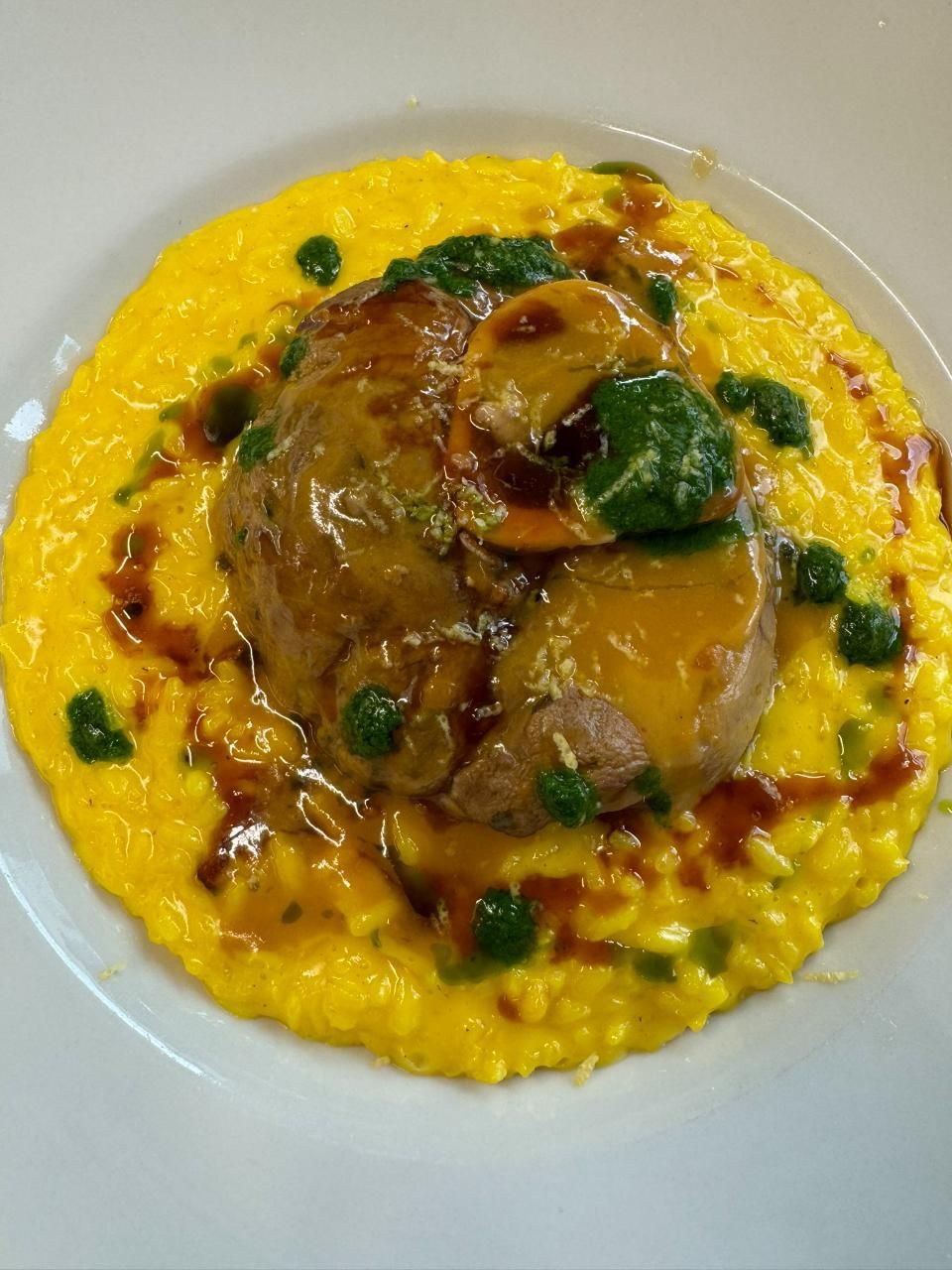 Ossobuco auf Safranrisotto, garniert mit einer grünen Sauce und brauner Glasur.