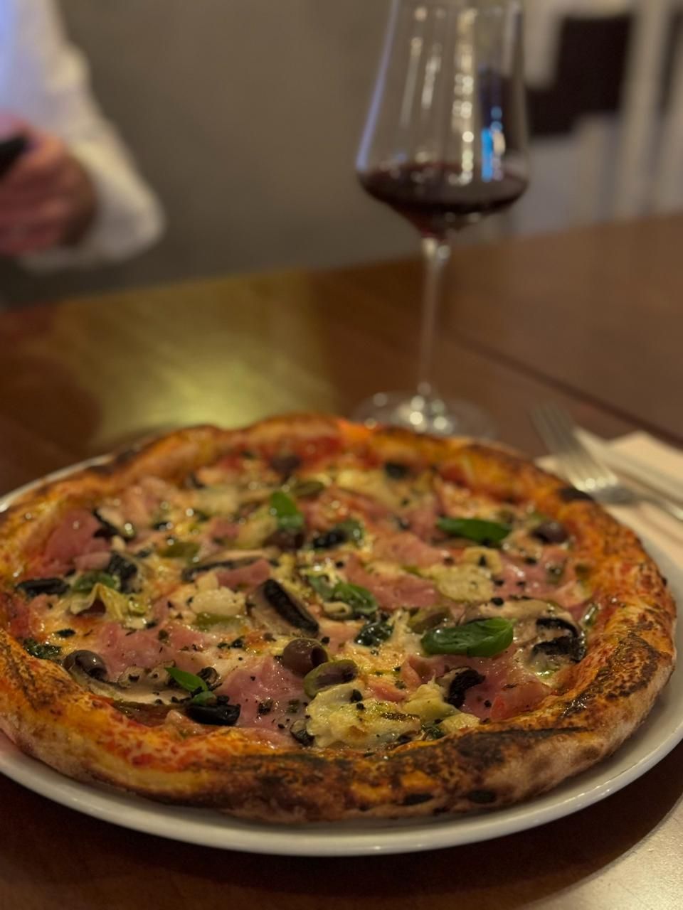Pizza mit Schinken und Champignons, ein Glas Rotwein auf dem Tisch.