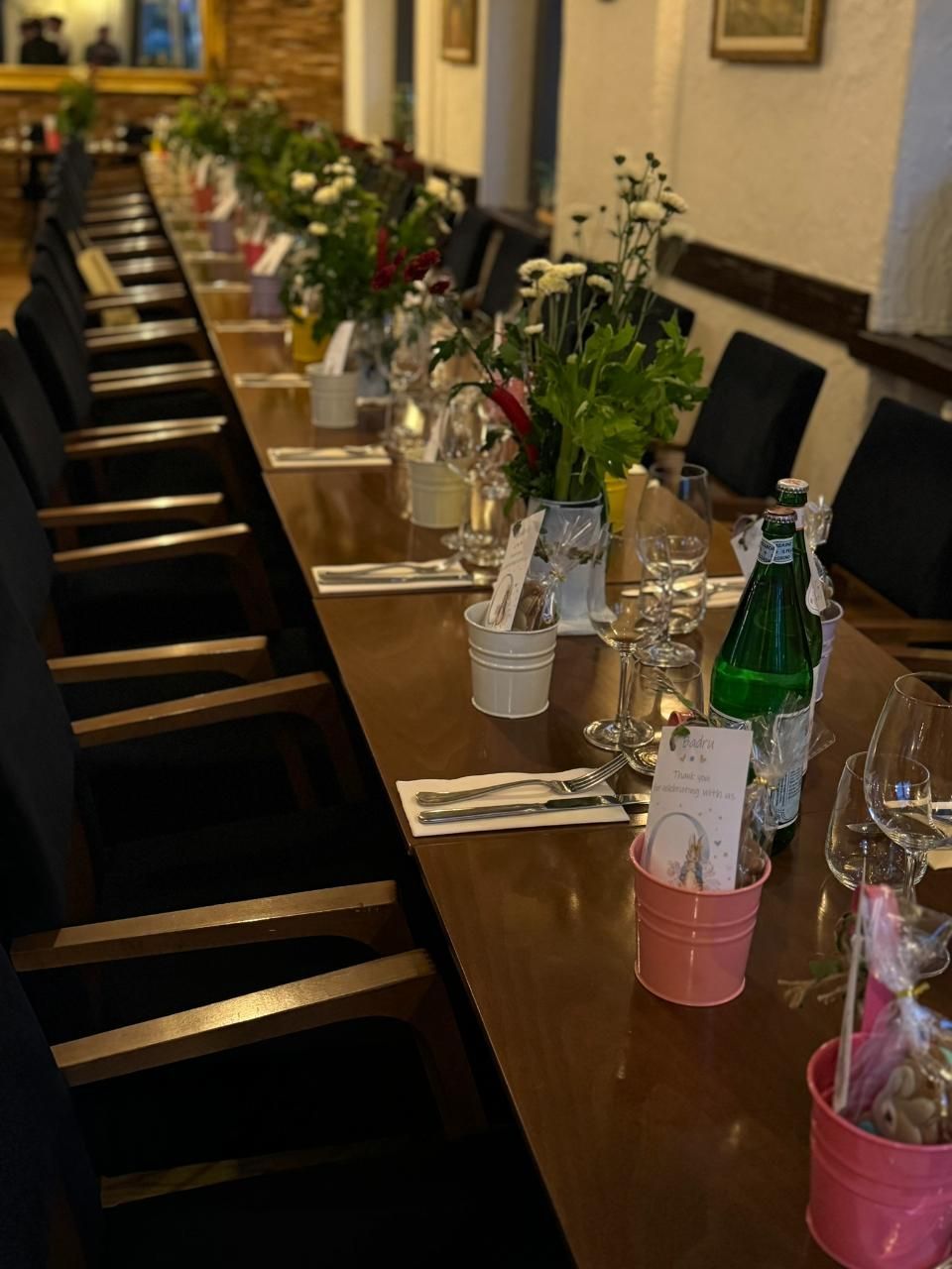 Ein langer Holztisch, gedeckt für ein Abendessen mit Blumenarrangements und Gedecken.