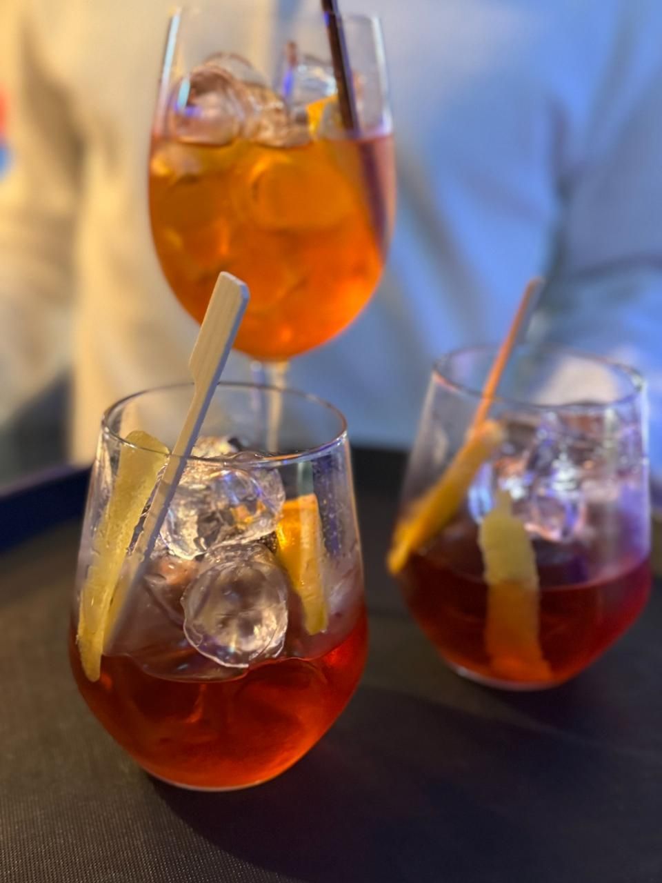 Drei Cocktails mit Eis, Orangenscheibe und Strohhalmen auf einem Tablett. Einer ist orange, die anderen rot.