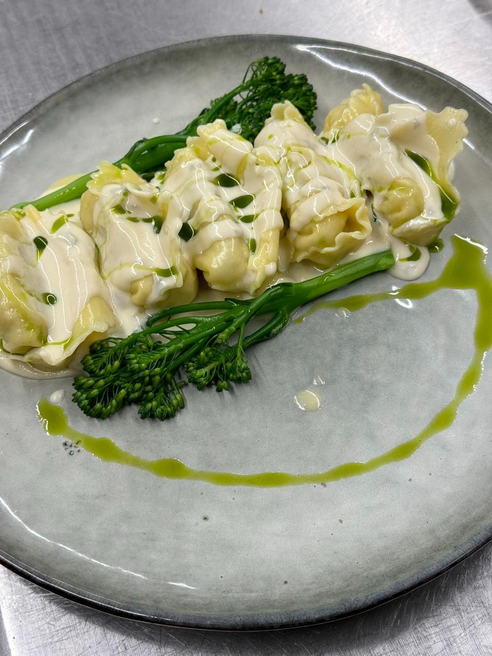 Tortellini mit Sahnesauce und Brokkoli auf einem grauen Teller, beträufelt mit grünem Öl.