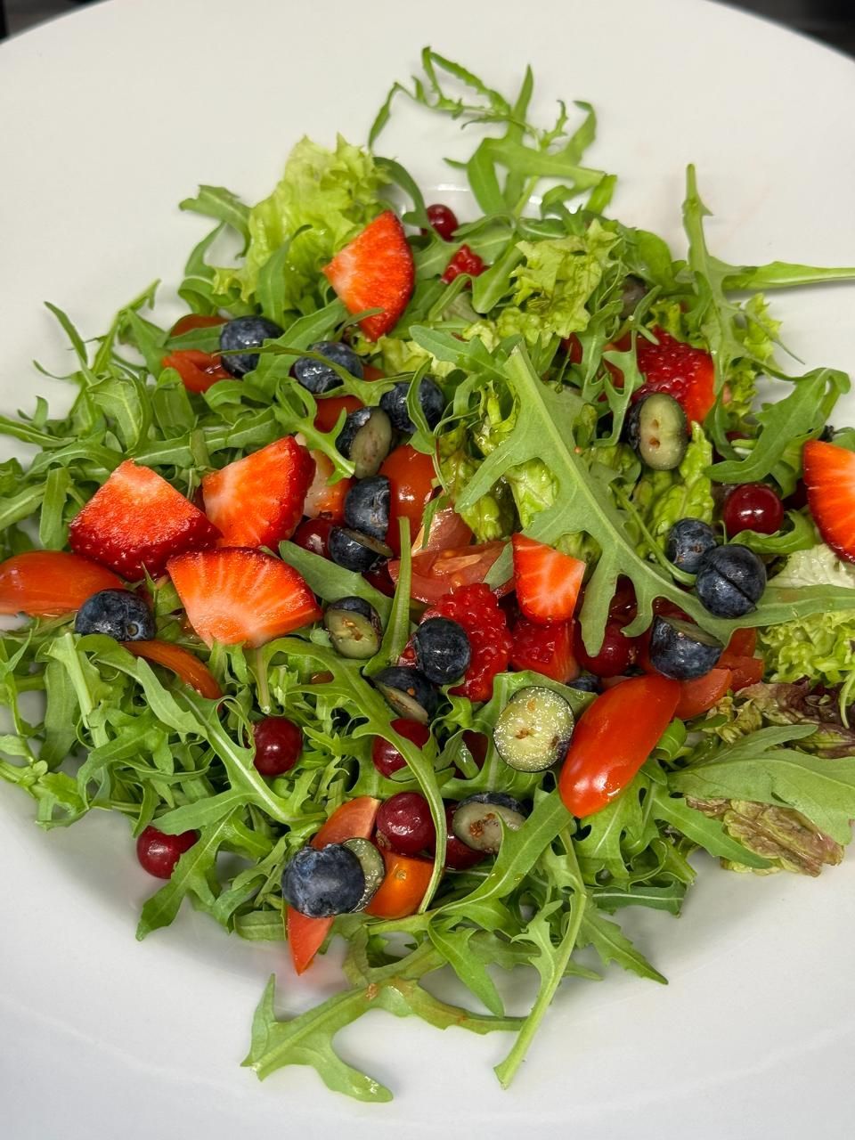 Salat mit Erdbeeren, Blaubeeren und gemischtem Blattgemüse auf einem weissen Teller.