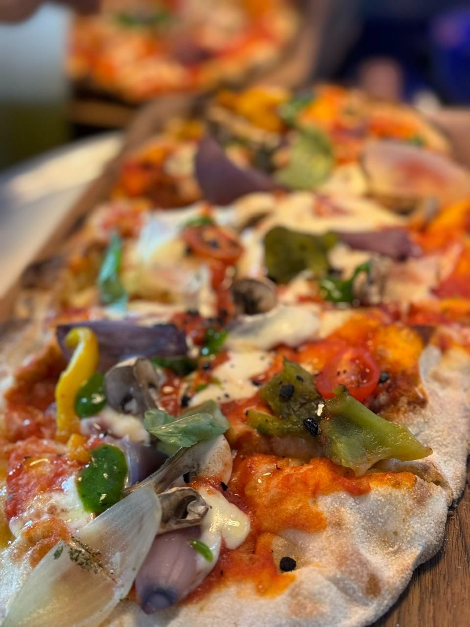 Gemüsepizza mit roter Sosse, Käse, Paprika, Zwiebeln und Champignons auf einem Holzbrett.
