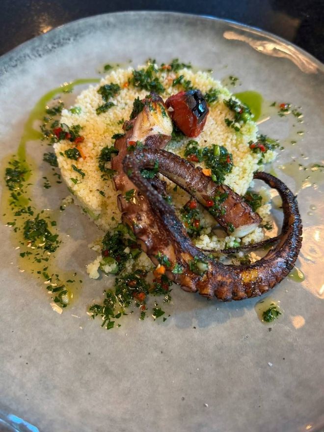 Gegrillte Oktopus-Tentakel auf einem Bett aus Couscous, mit Kräuteröl beträufelt und garniert.