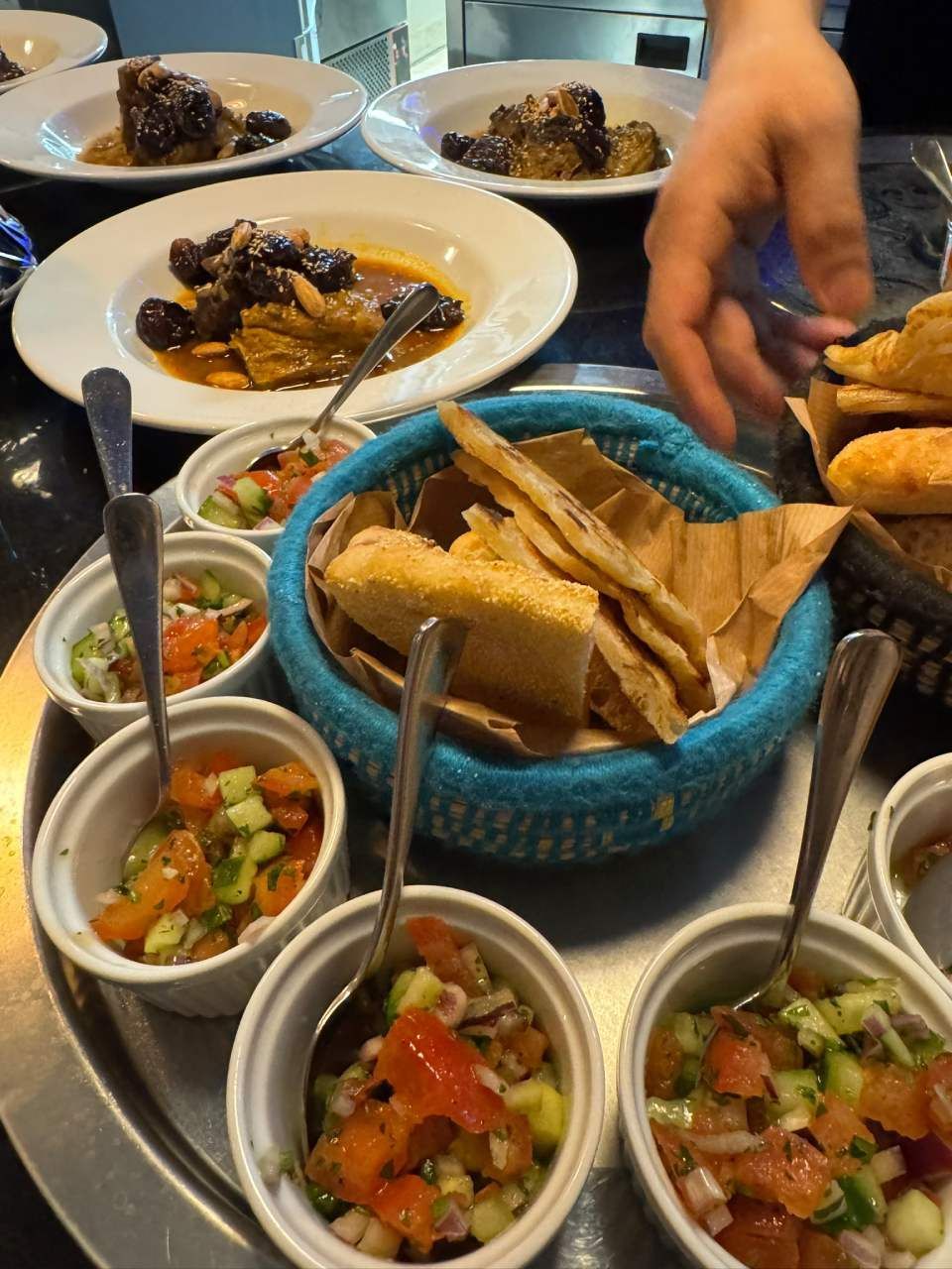 Ein Tisch mit kleinen Schälchen Salsa, Tortilla-Chips und Tellern mit geschmortem Fleisch. Jemand greift nach einem Chip.