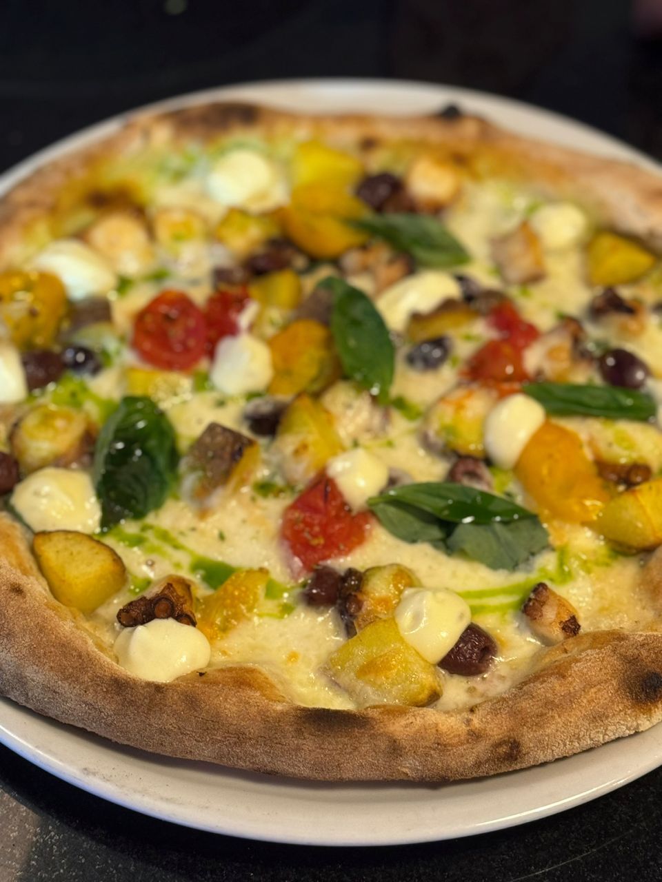 Pizza belegt mit gelben und roten Tomaten, Mozzarella, Basilikum und beträufelter Sauce.