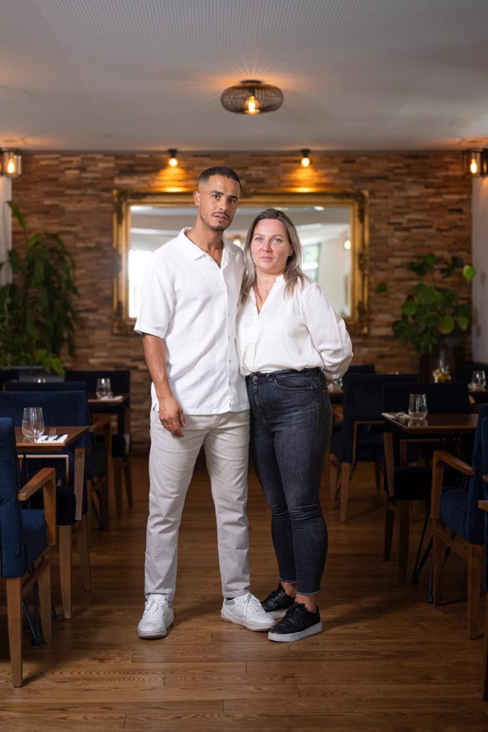 Zwei Personen, ein Mann und eine Frau, stehen in einem Restaurant. Sie umarmen sich vor einem grossen Spiegel.