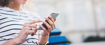 Una mujer está sentada en un banco usando un teléfono celular.