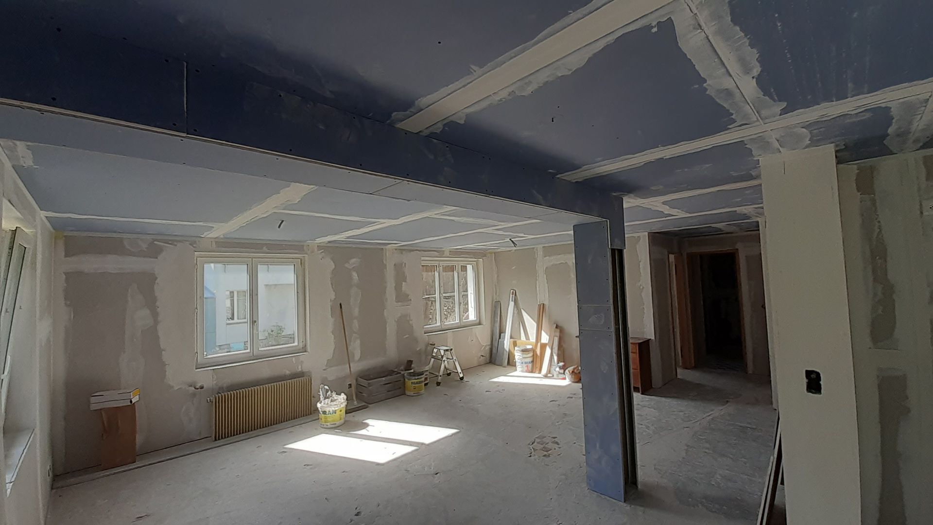Pièce rénovée vide avec cloisons sèches blanches, plafond mansardé, fenêtre et ouverture de porte
