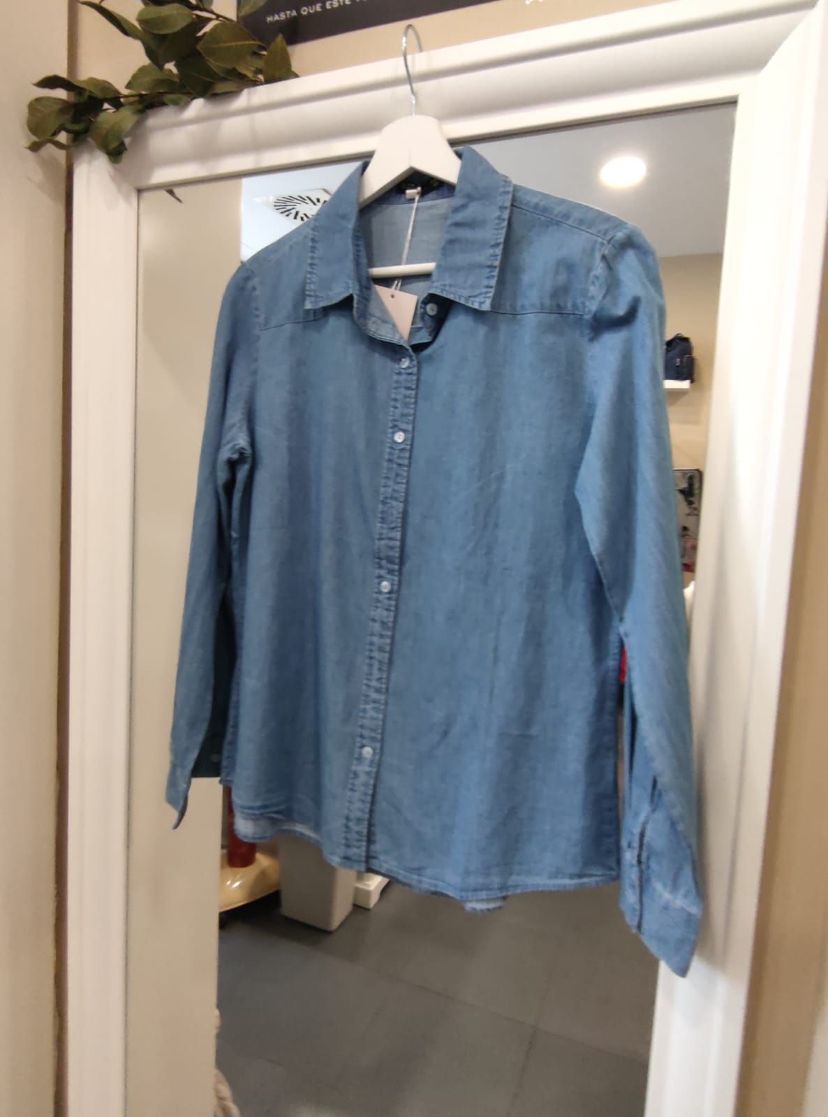 Una camisa vaquera azul está colgada en una percha frente a un espejo.