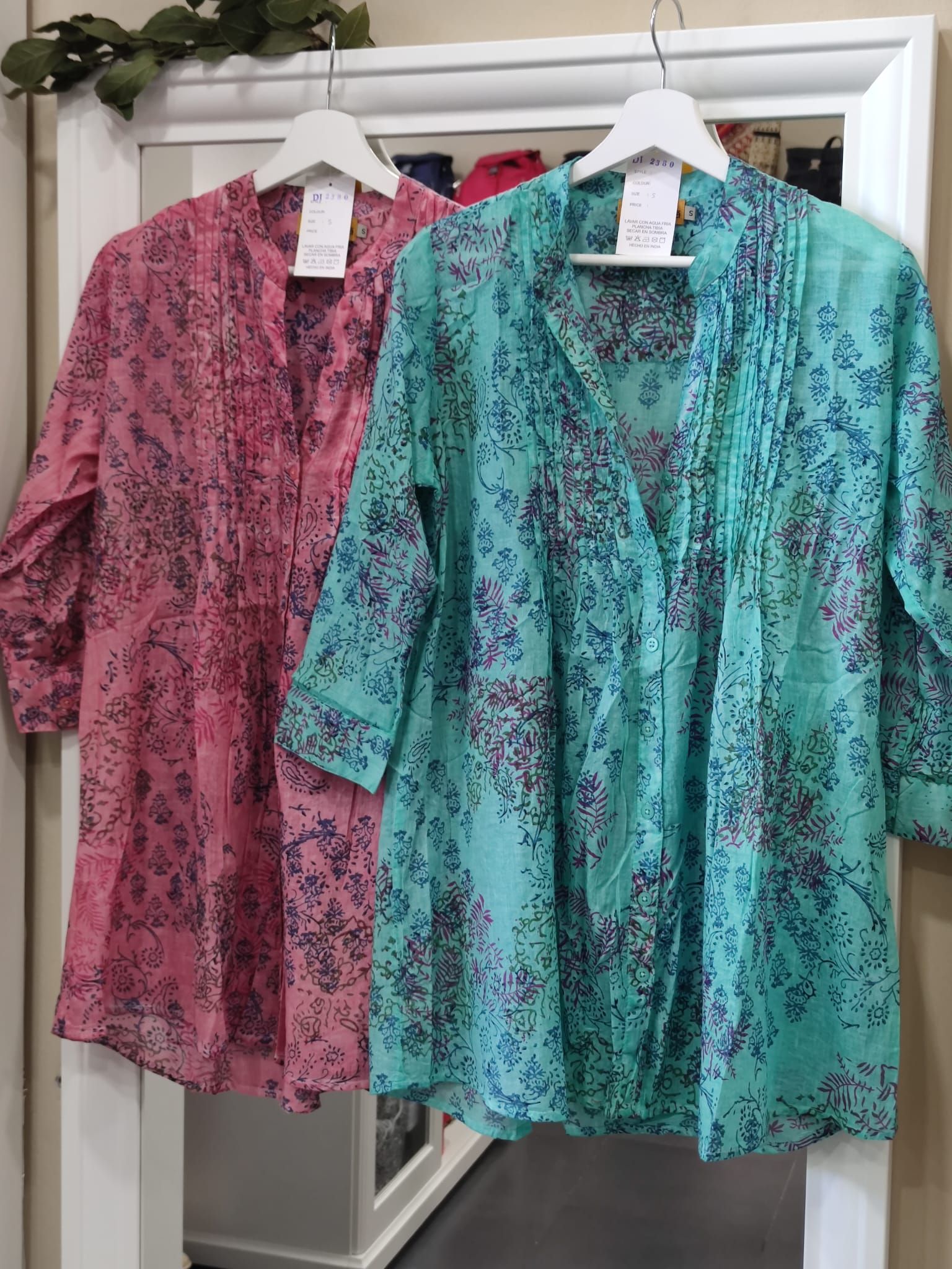 Dos camisas están colgadas en un perchero frente a un espejo.