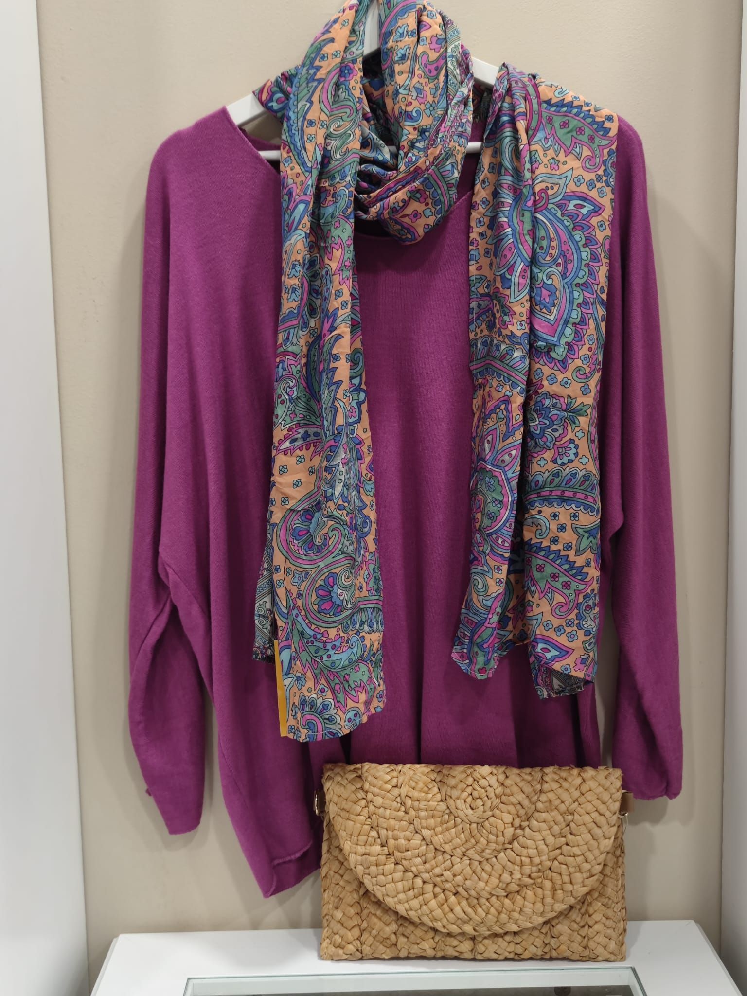 Un suéter morado con una bufanda y un bolso colgado en una percha.