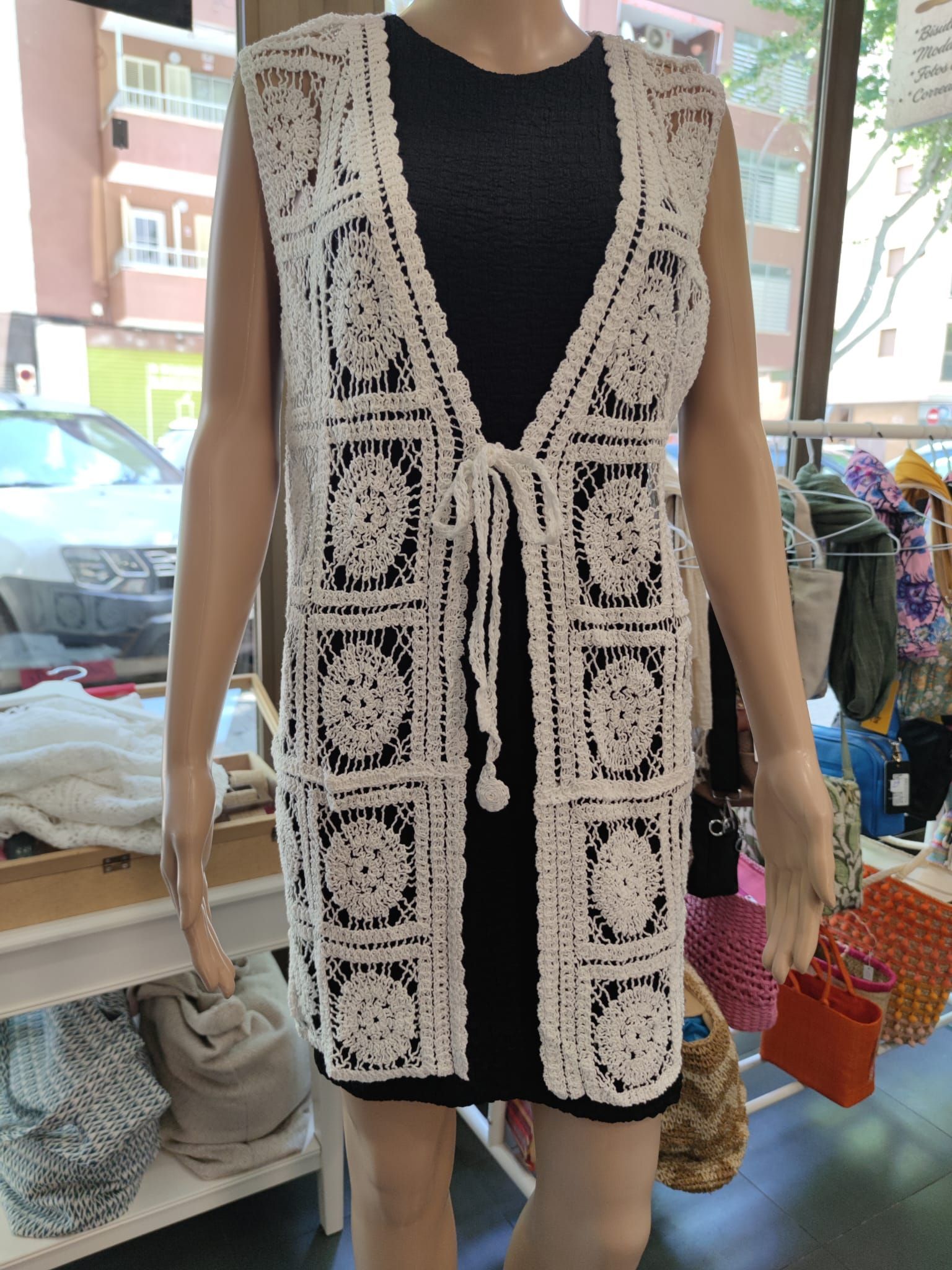 Un maniquí lleva un chaleco de encaje blanco y un vestido negro.