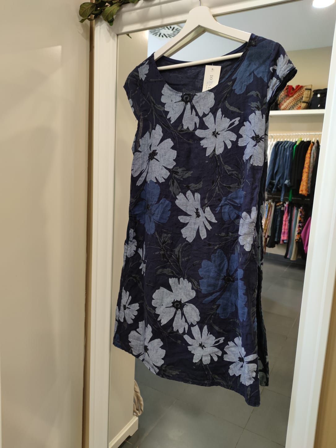 Un vestido floral azul cuelga de una percha frente a un espejo.