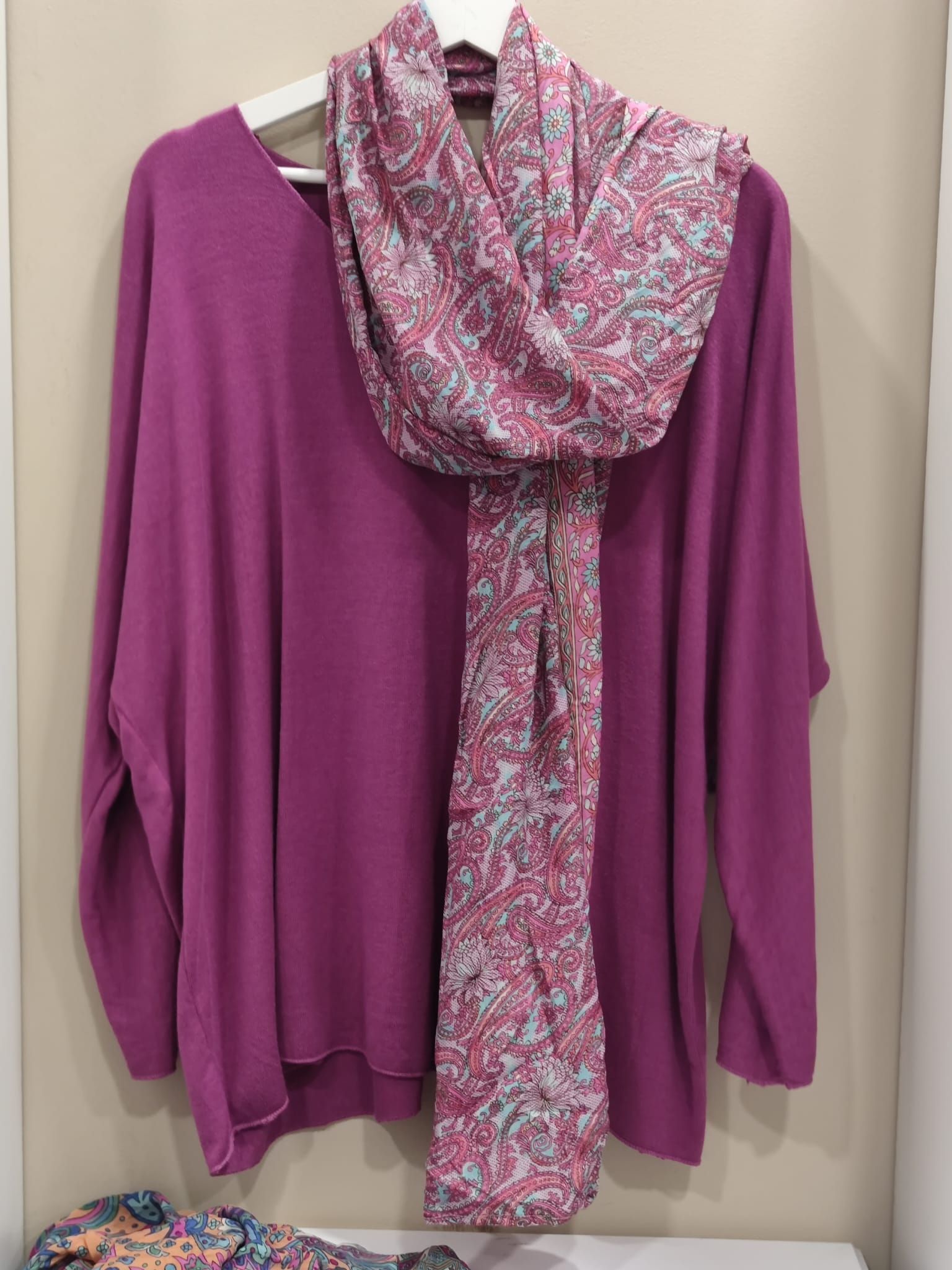 Un suéter morado y una bufanda rosa cuelgan de una percha.