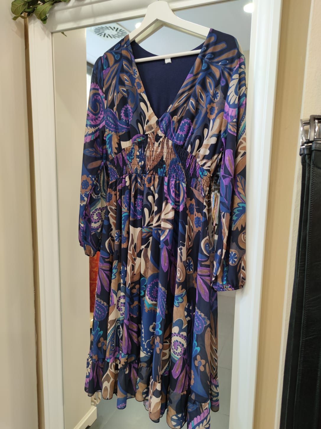 Un vestido morado cuelga de una percha frente a un espejo.