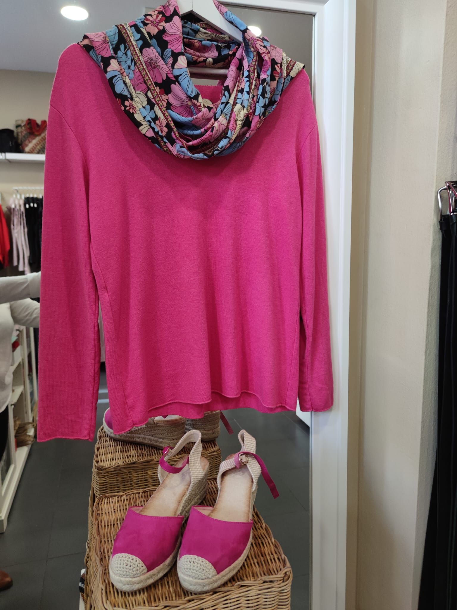 Un suéter rosa, una bufanda y zapatos están en exhibición en una tienda.