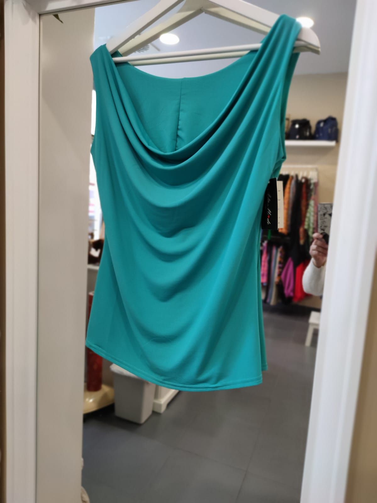 Una camiseta verde está colgada en una percha frente a un espejo.