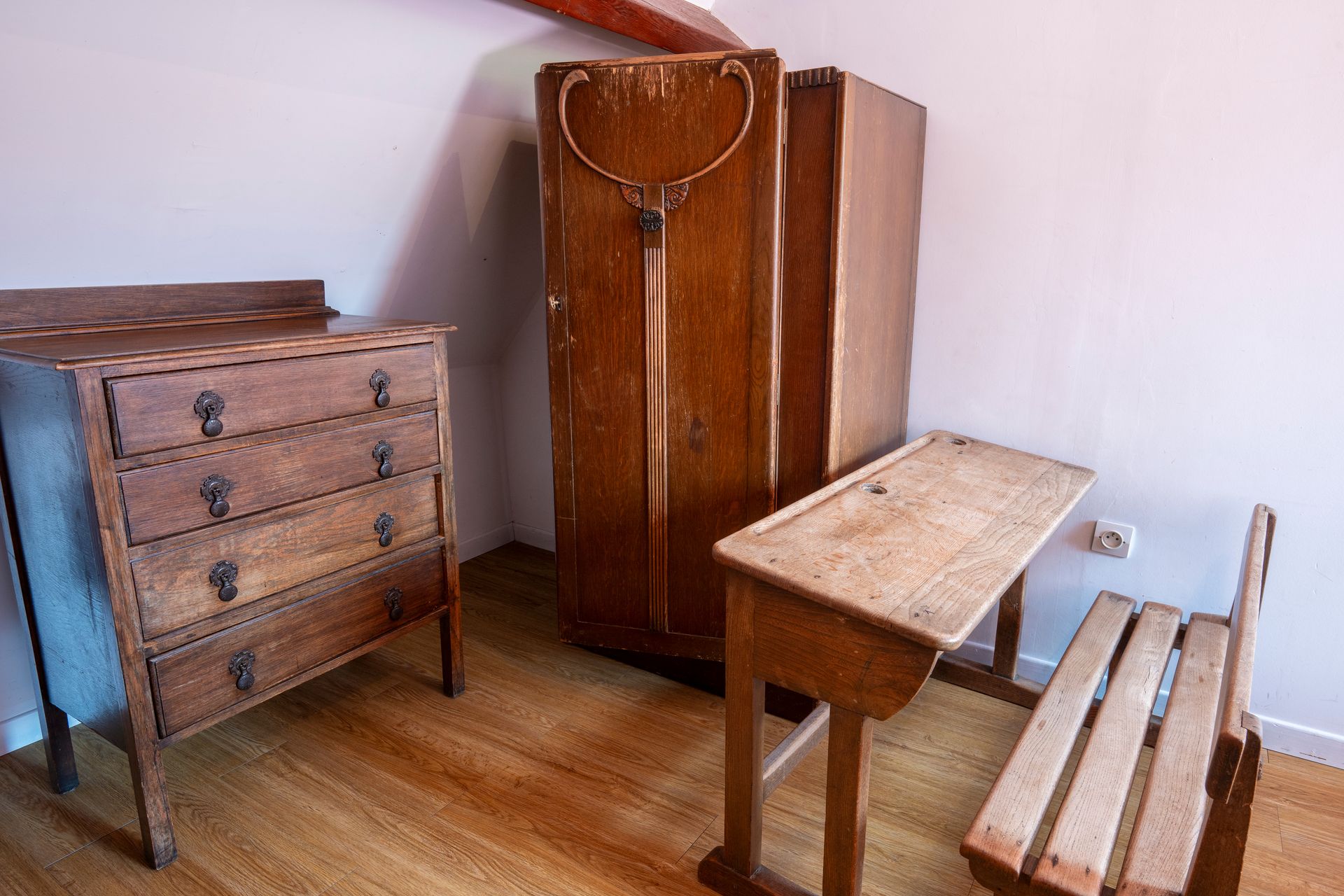 Ensemble de meubles vintage en bois dans une pièce : commode, armoire, table, banc et tabouret sur un parquet.