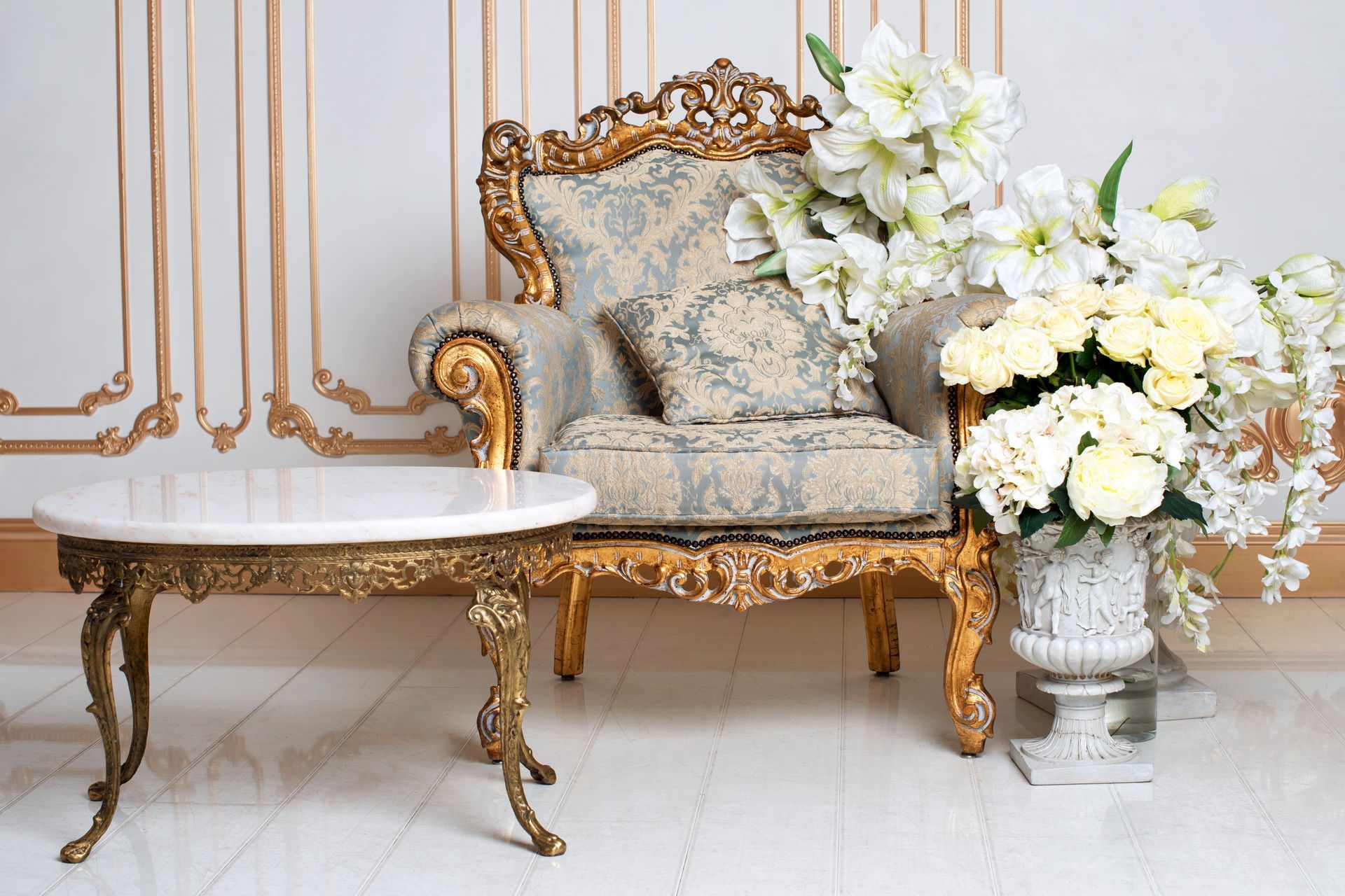 Fauteuil orné de dorures à côté d'une table en marbre et d'un arrangement floral blanc dans une pièce élégante