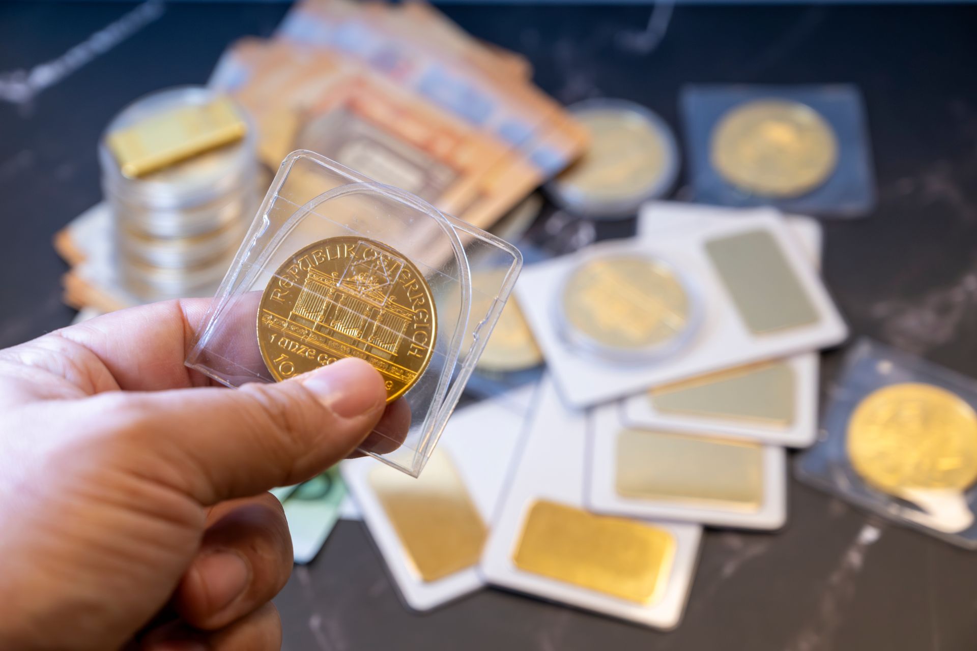 Main tenant une pièce dorée dans une capsule transparente, d'autres pièces et étuis étant éparpillés sur une table.