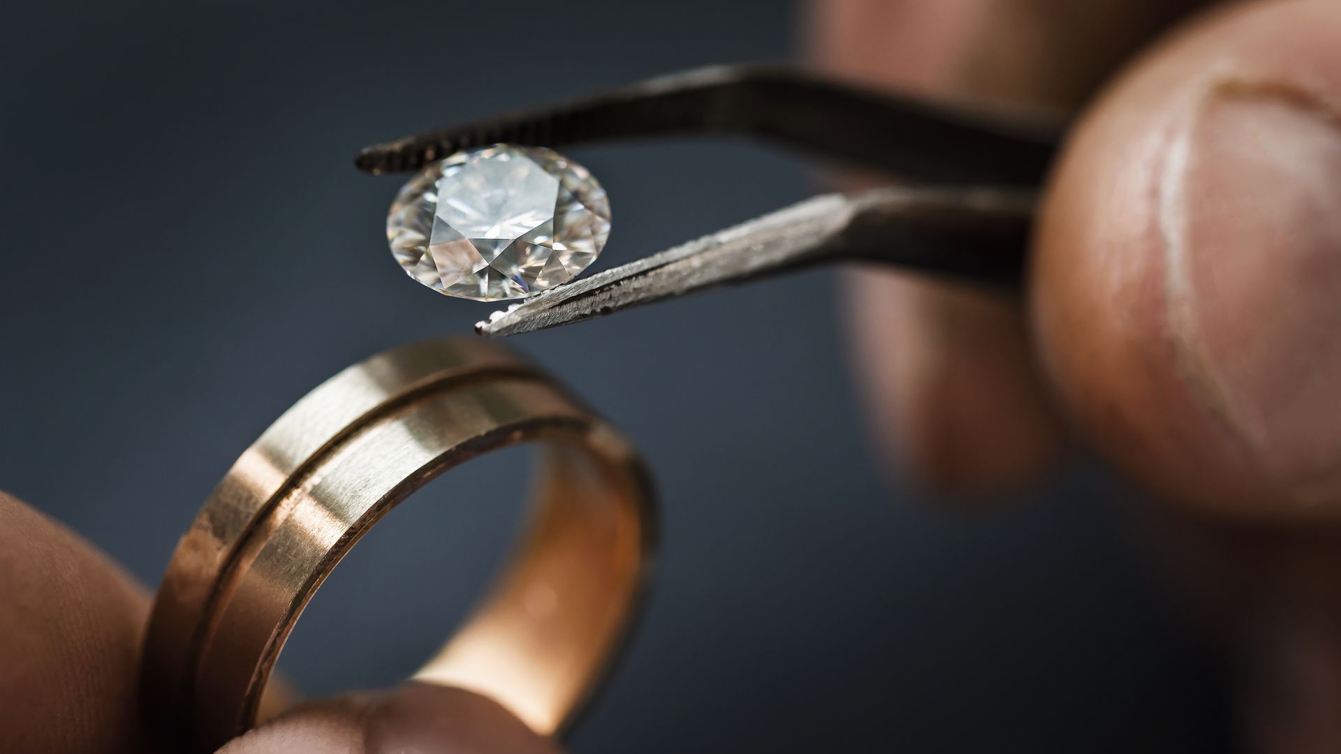 Main tenant une bague en diamant avec une pince à épiler à côté d'une alliance en or