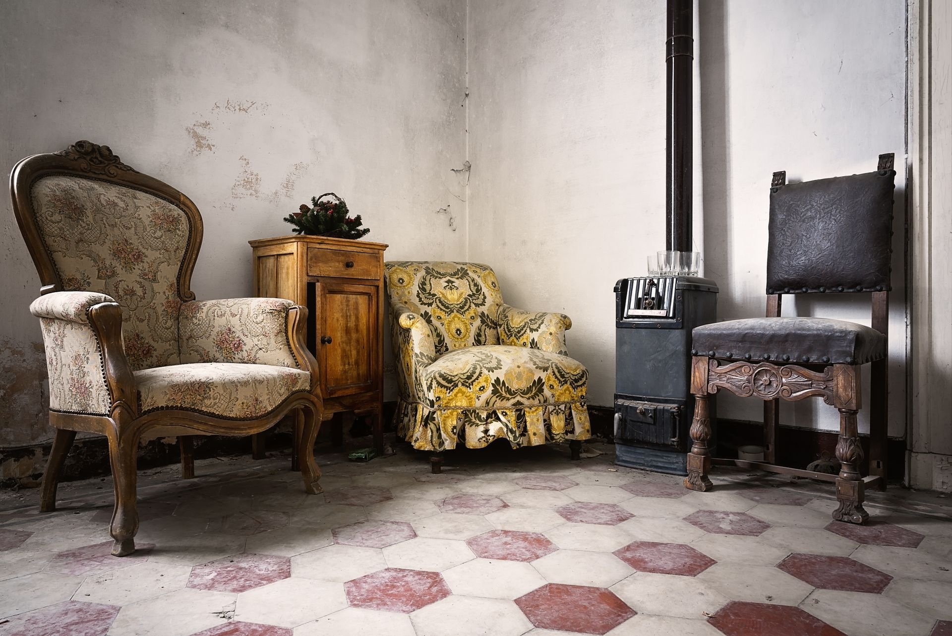 Pièce à l'ancienne avec quatre fauteuils dépareillés, une petite armoire en bois et un sol carrelé à motifs