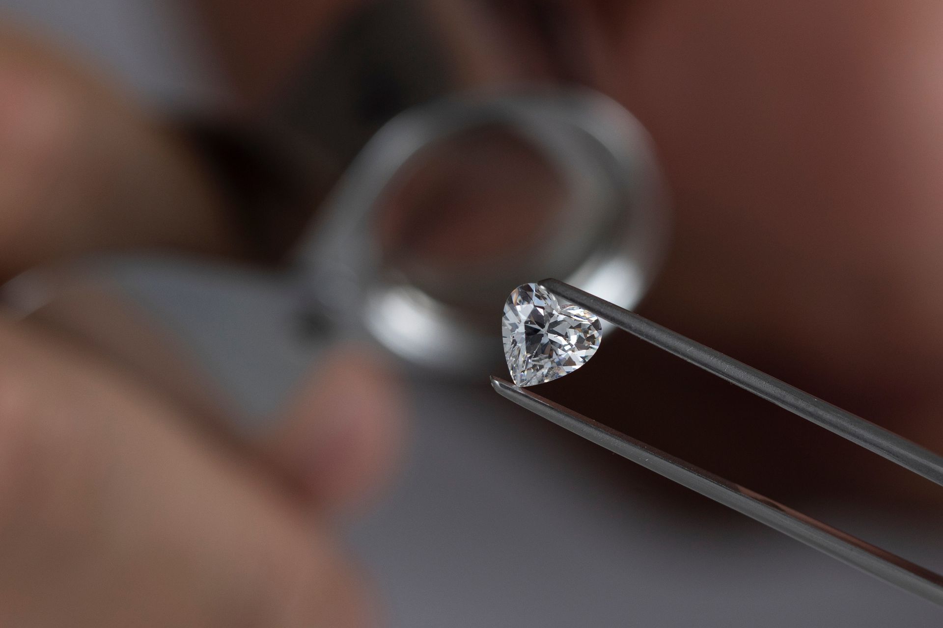 Une pince à épiler tenant une pierre précieuse transparente à facettes près d'une monture de bague