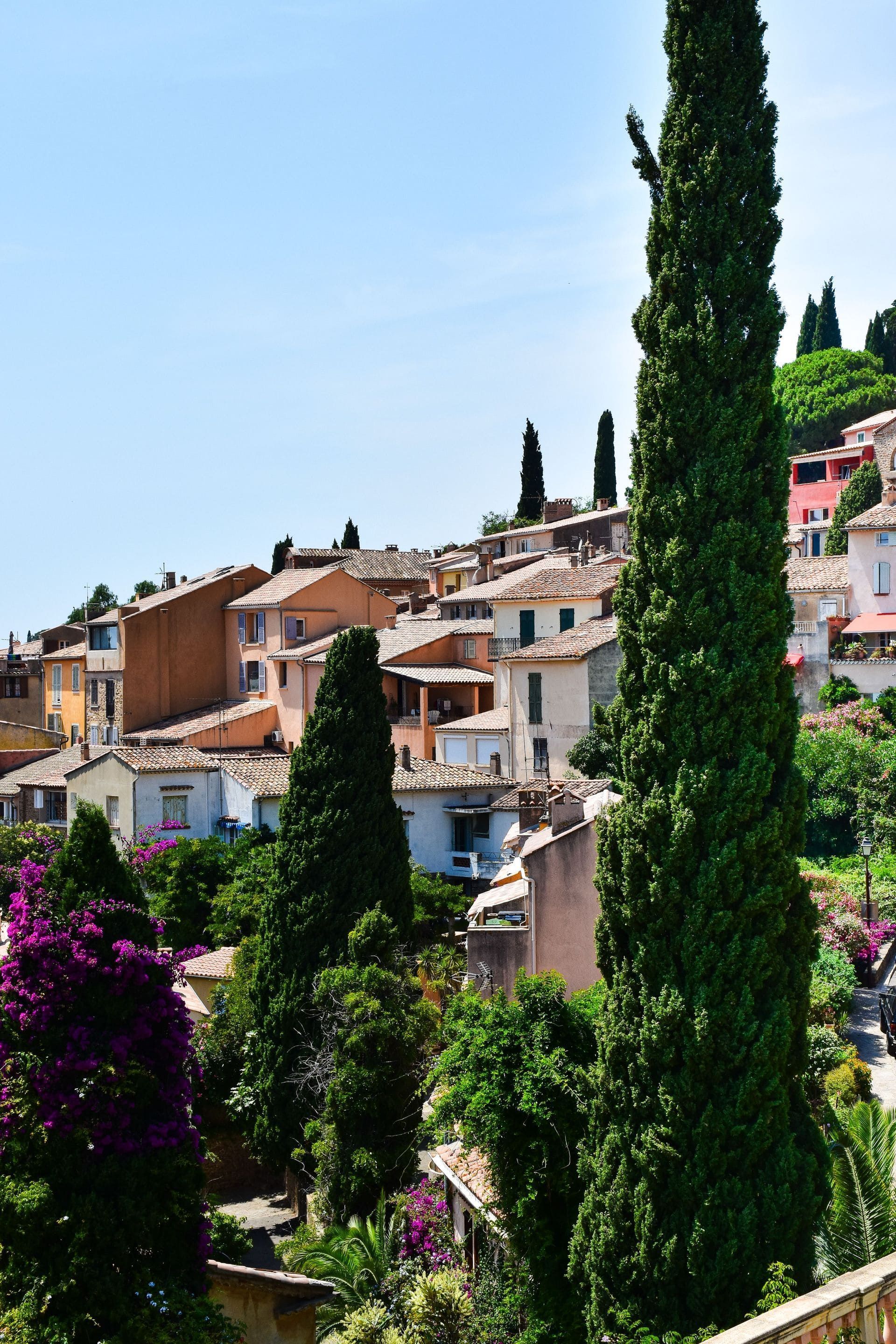 Village pittoresque à flanc de colline, avec ses maisons en terre cuite et ses grands cyprès sous un ciel bleu
