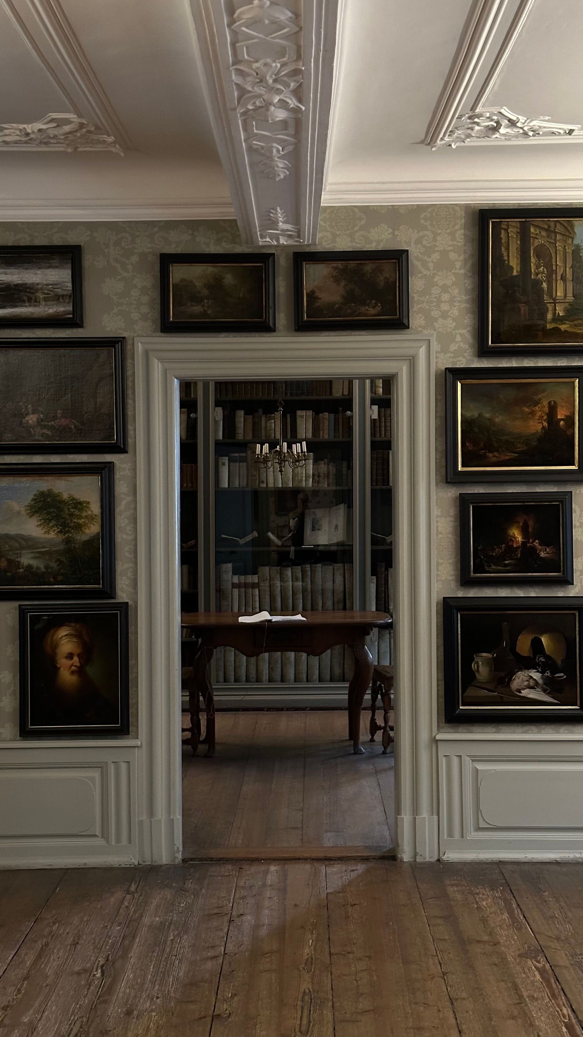 Pièce élégante avec tableaux encadrés, murs lambrissés blancs, plafond orné et porte ouverte sur une salle à manger